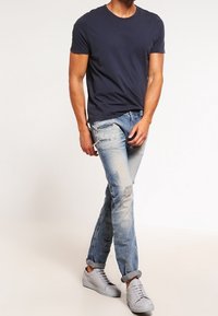 Marinblå bomullströja i kombination med slitna ljusblå jeans och grå sneakers. Jeansen har revor och en uppvikt fåll.