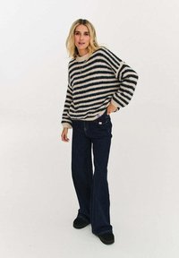 Sweter w paski w kolorze kremowym i granatowym, o luźnym kroju i ściągaczach przy mankietach, zestawiony z ciemnymi rozszerzanymi dżinsami i czarnymi wsuwanymi butami.