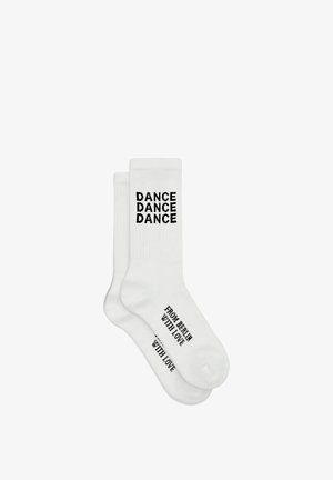 Weiße Sportsocken mit Bündchen, auf denen oben vertikal "DANCE DANCE DANCE" und auf dem Fuß in schwarzer Schrift "FROM BERLIN WITH LOVE" gedruckt sind.