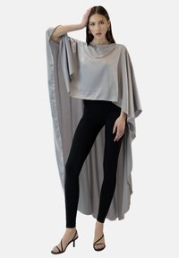 Ljusgrå satinöverdimensionerad poncho med flödande ärmar, lager-på-lager-design, kombinerad med svarta leggings och remklackar. Mjuk textur.