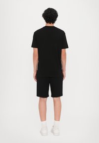 Svart bomull t-skjorte med korte ermer, kombinert med matchende svarte shorts. Hvite joggesko og synlige ankelstrømper fullfører antrekket.