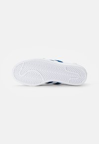 White sneaker sole with a textured grip pattern. Blue fabric upper visible along the sides and rear with contrasting white stripes.