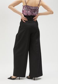 Zwarte brede beenbroek met een hoge taille, voorzien van zijzakken en een gladde stof. Gestyled met een gewatteerd roze top en spitse zwarte schoenen.