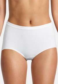 Frau trägt weiße hochtaillierte Baumwollslips, die den Bauch und die Oberschenkel zeigen, vor einem neutralen Hintergrund.