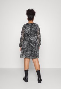 Vestido negro con flores, mangas largas transparentes, cintura ajustada y falda acampanada, combinado con botas negras gruesas hasta el tobillo.