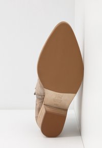 Botín de ante beige con tacón cónico, suela texturizada y detalle de cremallera. Etiqueta interior de cuero grabada que indica talla 41.5.