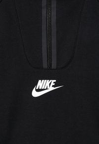 Zwarte sweatshirt met een kraag met rits van een kwart, voorzien van een zilveren Nike-logo op de borst en een gladde, gestructureerde stof.
