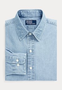 Jasnoniebieska koszula dżinsowa, kołnierz zapinany na guziki, długie rękawy z mankietami na guziki, białe guziki i subtelna tekstura. Metka marki: Polo by Ralph Lauren.