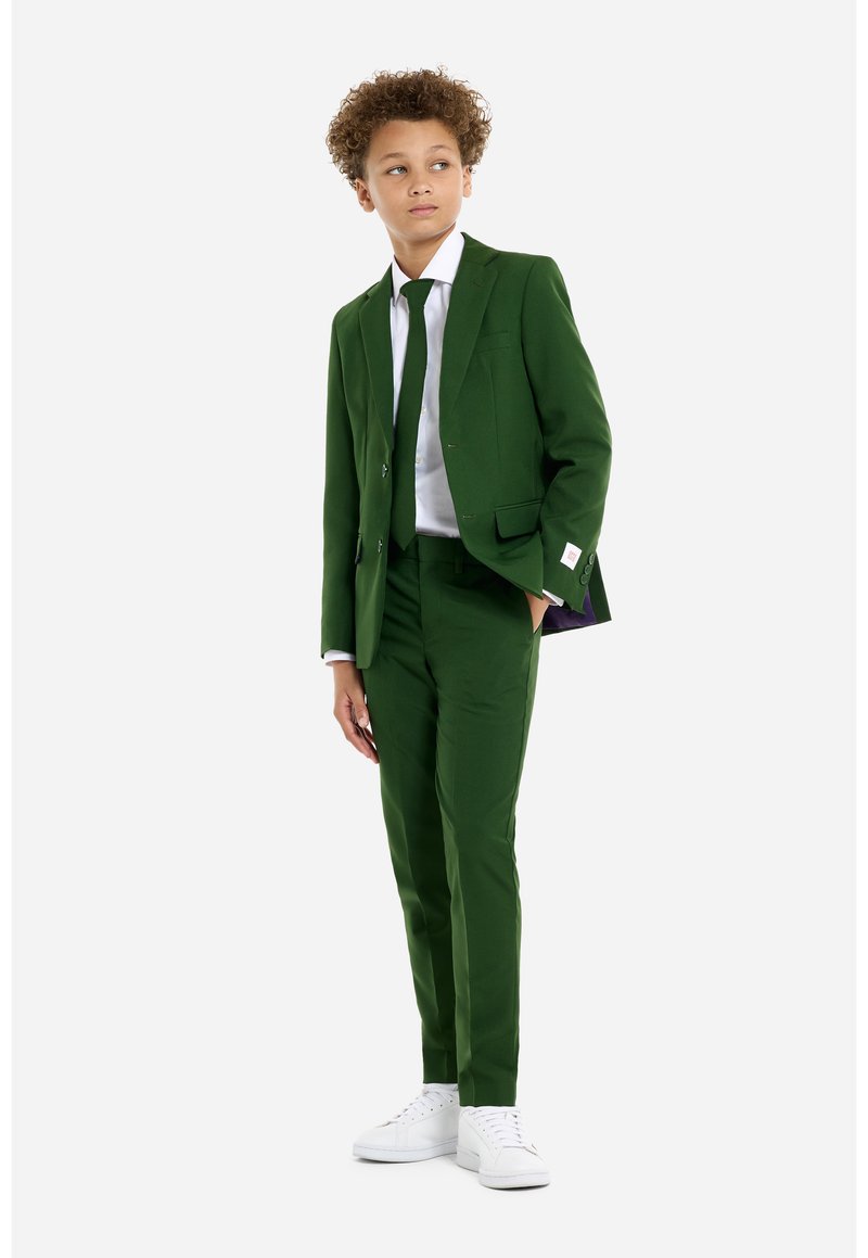 Completo verde con due bottoni, slim fit, abbinato a una camicia bianca e una cravatta coordinata. Sneakers bianche completano il look. Tessuto strutturato, design moderno.