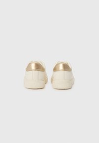 Weiße Sneakers mit glänzendem goldfarbenem Fersenakzent, aus glattem Material, mit abgerundeter Form und einer strukturierten Sohle, die mit "TOMMY HILFIGER" gekennzeichnet ist.