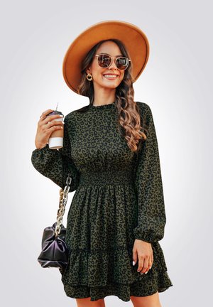 Vestido verde de estampado de leopardo con mangas largas y cintura fruncida; combinado con un sombrero de ala ancha en tono beige y gafas de sol redondas. Bolso negro y café.