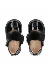 Scarpe in vernice nera con punta arrotondata, decorate con un nastro nero a forma di fiocco e un pompon in pelliccia sulla parte anteriore. Dettagli in metallo color oro.