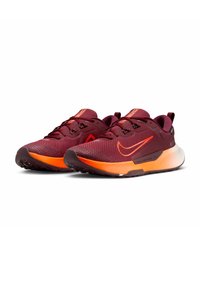 Une paire de chaussures de course bordeaux avec des semelles orange et le swoosh de Nike, présentée sur un fond blanc, légèrement inclinée vers la gauche.