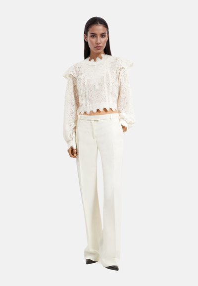 Witte kanten crop top met gerimpelde mouwen en gekartelde zoom, gecombineerd met witte hoge taille broek; soepel materiaal en getailleerde pasvorm.