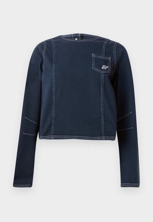 Mørkeblå cropped top lavet af denim, med lange ærmer, hvid syning og en brystlomme med et logo. Enkel, struktureret design.