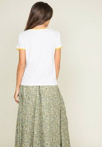 T-shirt blanc avec des bordures jaunes, associé à une longue jupe verte à motifs floraux blancs et jaunes. Tissu doux et coupe décontractée.