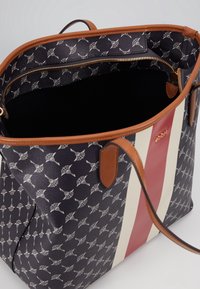 Taška typu tote s tmavě modrým vzorovaným povrchem s bílými akcenty, červeno-krémovými pruhy, hnědými koženými držadly a vnitřní kapsou na zip.