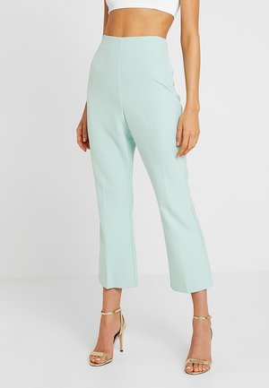 Mintgroene hoge taillebroeken gemaakt van gladde stof, met een rechte pijp en minimale naden, gecombineerd met gouden sandalen met bandjes.