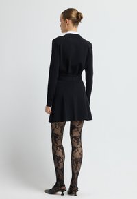 Černý top s dlouhými rukávy, přiléhavý pas, plisovaná černá sukně, průhledné černé punčochy s květinovým vzorem a černé špičaté boty s nízkým podpatkem.