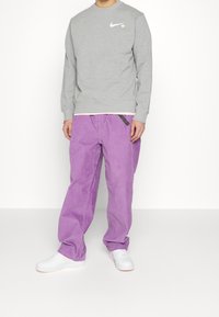 Grå sweatshirt med en vit Nike-logotyp, kombinerad med löst sittande, lila bomullsbukser med svart snodd och vita sneakers.