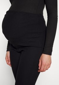 Legginsy ciążowe w czarnej, prążkowanej tkaninie, z wysokim stanem, gładką strukturą i dopasowanym krojem, zapewniające wsparcie w okolicy brzucha.