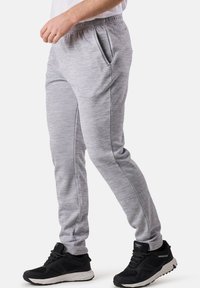 Graue sportliche Jogginghosen mit glatter Textur, elastischem Bund, Seitentaschen und tailliertem Design; getragen mit schwarzen Sportschuhen.