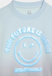 Sudadera azul claro con un diseño de cara sonriente brillante y el texto "EL FUTURO ESTÁ AQUÍ" en letras elevadas y con forma de burbuja.