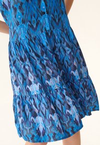 Vestido de estampado azul con un diseño en capas, tejido ligero, detalles de botones y patrones abstractos intrincados en diferentes tonos de azul.