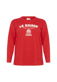 T-shirt rouge à manches longues avec un col rond, affichant un texte blanc qui dit "LA MAISON VOTRE LIEU PRÉFÉRÉ" et un imprimé d'emblème. Matière en coton doux.