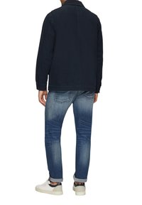 Navy Baumwolljacke mit crispem Kragen, knöpfbaren Manschetten und einem schlichten Rückendesign, kombiniert mit hellblauen Jeans und weißen Sneakern.