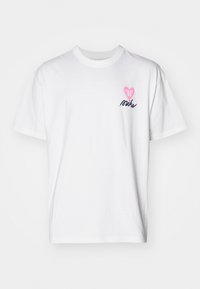 Camiseta de algodón blanca de manga corta, con un logo en forma de corazón rosa y la palabra "Nike" en azul marino, situada en el área del pecho izquierdo.