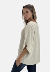 Blusa oversize color crema con una texture morbida, maniche ampie e scollatura rotonda, abbinata a jeans in denim scuri.