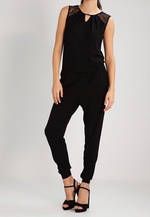 Combinaison noire avec un décolleté en trou de serrure et des accents en dentelle aux épaules. Tissu doux avec une coupe décontractée et des jambes fuselées.