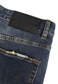 Donkerblauwe denim jeans met een achterzak met gele stiksels en een zwart merkembleem op de tailleband.