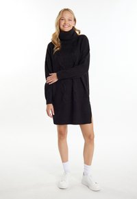 Abito nero a maglia con collo alto, caratterizzato da un motivo a trecce testurizzato, polsini e orlo a costine, abbinato a sneaker bianche e calze.