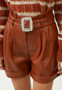 Braune Kunstleder-Shorts mit Falten, ausgestattet mit einem breiten Gürtel mit einer großen, mit Kristallen besetzten Schnalle. Umgeschlagener Saum.