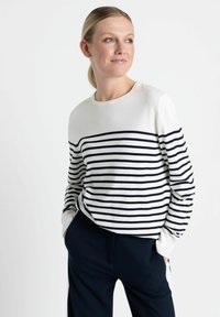 Weißer Pullover mit marineblauen horizontalen Streifen, rundem Ausschnitt und gerippten Bündchen, kombiniert mit marinen Hosen. Glattes Material, lockere Passform.
