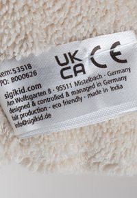 Helle, plüschartige Stoffoberfläche mit einer weichen, strukturierten Textur. Enthält ein Pflegeetikett mit schwarzem Text, einschließlich CE- und UKCA-Kennzeichnungen.