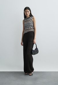 Mönstrad tanktopp i flera färger med rund halsringning, svarta vida byxor med vågig textur och en liten mönstrad handväska.