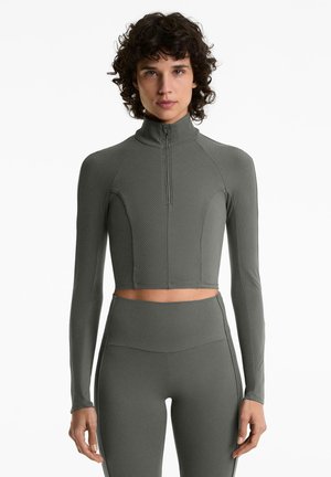 Grijze cropped zip-up top met lange mouwen en ribbelstructuur, gecombineerd met hoge taille leggings in dezelfde stijl. Soepele, rekbare stof.