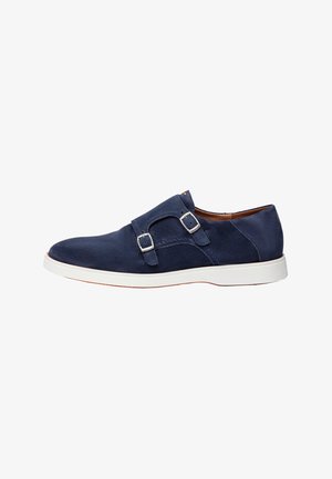 Zapato de vestir de hombre de ante azul marino con hebillas de doble correa monk y suela de goma blanca, vista lateral sobre fondo blanco.