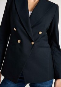 Sort dobbeltradet blazer i tekstureret stof med seks guldfarvede knapper og spidse revers, designet med en afslappet pasform.