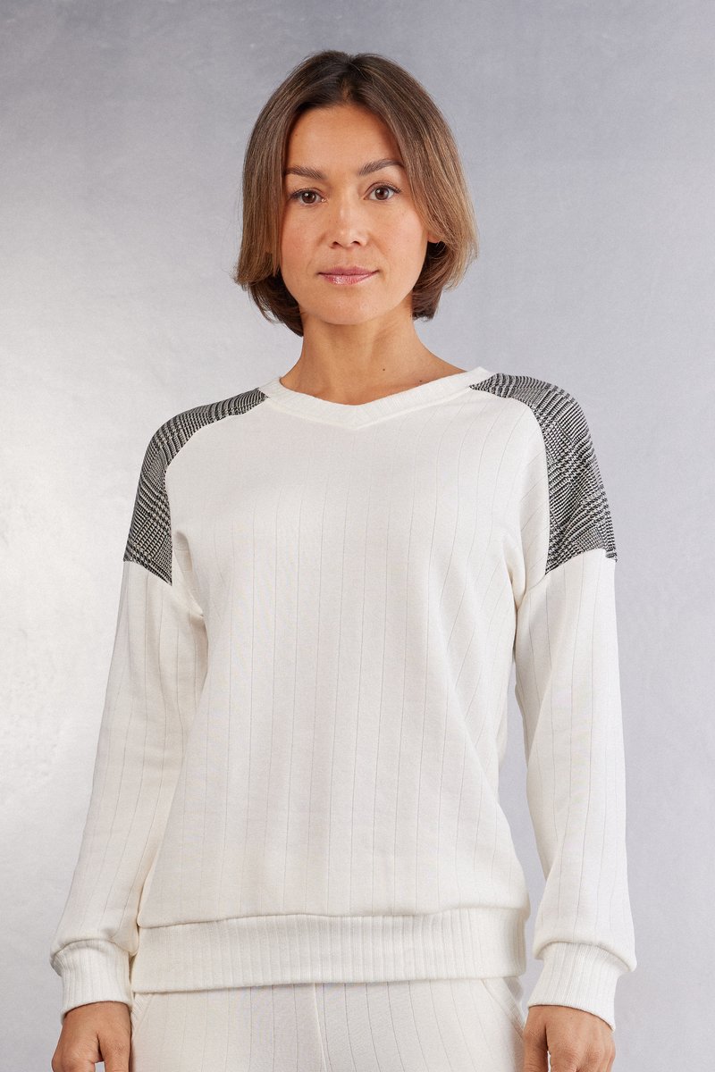 Vit ribbad sweatshirt med V-ringning, som har strukturerade axelpartier i svart och vitt mönster samt ribbade ärmslut och fåll.