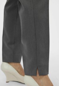Pantaloni grigi su misura con una vestibilità affusolata, dotati di uno spacco all'orlo, abbinati a comode décolleté bianche con zeppa.