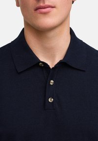 Námořnická modrá polo košile z texturované látky, s klasickým límcem a třemi knoflíky na léga se světlými knoflíky.