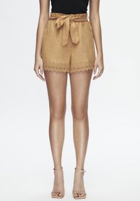 Pantaloni corti di lino beige con vita a cintura e orlo rifinito con pizzo scallopato. Abbinati a sandali con tacchi beige.
