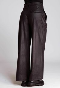 Person wearing high-waisted, wide-leg black leather pants and black platform shoes, standing against a plain light background.