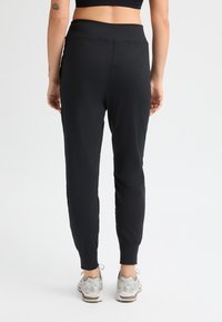 Pantalones joggers negros hechos de una tela suave y elástica, con una cintura alta y puños ajustados, combinados con zapatillas deportivas plateadas.