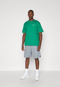 Green Nike t-shirt with short sleeves and crew neck, paired with light gray athletic shorts. White sneakers complete the outfit.