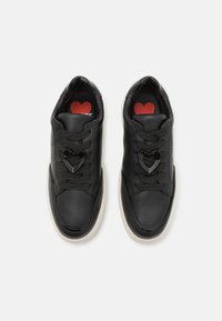 Melnas ādas sporta apavi ar sirds formas šoferiem, apaļu purngalu, auduma oderi, baltu gumijas zoli un sarkanu iekšējo zoli.